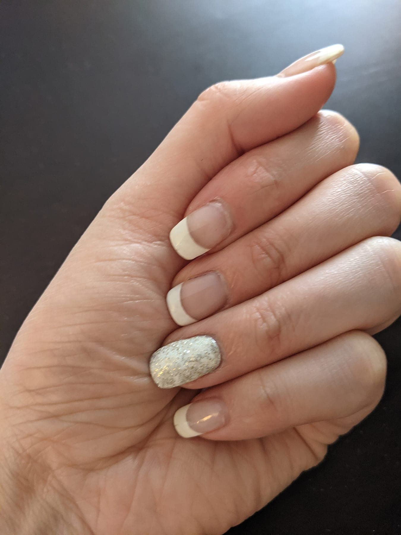 A hand with a glossy French manicure and a glitter accent nail